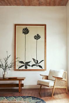 a painting hanging on the wall next to a chair and table with a plant in it