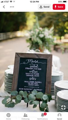 a table topped with plates and menus next to a chalkboard sign filled with greenery