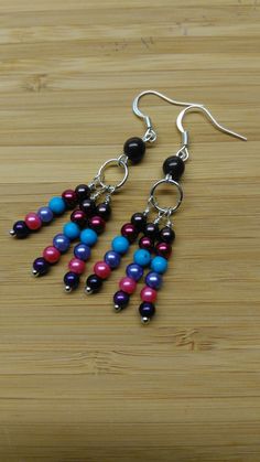 two pairs of colorful beads hanging from silver earwires on a wooden table top