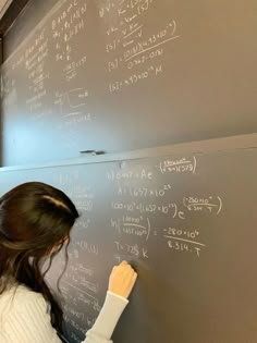 a woman writing on a blackboard in front of a wall with lots of chalk