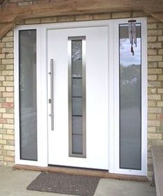 a white double door with glass panels on the side of a brick wall next to a wooden bench