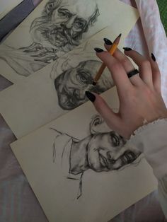 a woman's hand holding a pencil next to some drawings and a drawing of a man