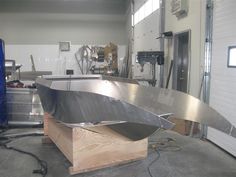 a large metal boat sitting on top of a wooden stand in a garage next to a blue tarp