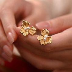 a woman is holding two gold flowers with pearls in their hands and they are both wearing matching rings