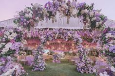 an outdoor wedding setup with purple and white flowers on the ceiling, draped in fabric