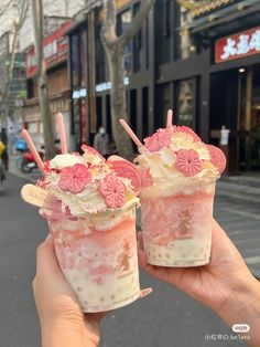 two ice cream sundaes with strawberries and flowers on top are being held up in the air