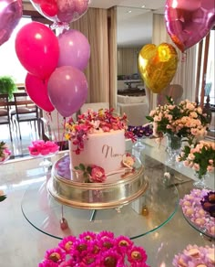 a cake with pink and gold balloons on it sitting on top of a glass table