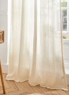 a white curtain hanging in front of a window next to a wooden table and chair