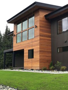 a modern house with wood siding and black trim on the windows, along with green grass