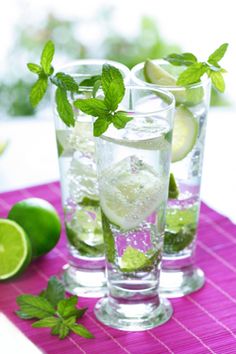 three glasses filled with water and limes on a pink place mat next to sliced limes