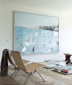 a living room filled with furniture and a painting hanging on the wall above it's glass coffee table