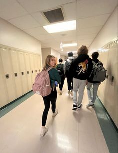 a group of people walking down a hallway next to lockers in a building with white walls