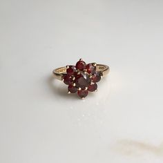 A Vintage 9 carat gold Garnet cluster ring. This beautiful piece holds a gorgeous collection of deep red stones in a gold setting, holding them high up on display. CONDITION: Wear consistent with age and use. Please see photos for more detail. HALLMARKED 9 CARAT GOLD, ASSAYED PRE 1975 STONE SIZE: 5mm (.50 carat) 3mm (.10 carat) SETTING DIAMETER: 12mm SETTING HEIGHT: 7mm BAND WIDTH: 1.5mm RING SIZE: UK: M | US: 6 1/4 WEIGHT: 3.0 grams (UZZ) Formal Cluster Ruby Ring, Classic Red Cluster Ruby Ring, Classic Red Ruby Cluster Ring, Red Cluster Ring Stamped 14k, Classic Cluster Ruby Ring, Red 14k Stamped Cluster Ring, Gold Ruby Cluster Ring, Gold Cluster Ruby Ring As Gift, Gold Cluster Ruby Promise Ring