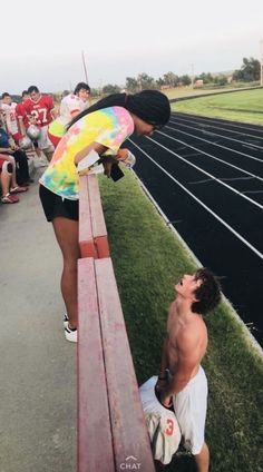 a man kneeling down next to a bench on top of a race track with other people watching