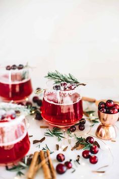 two glasses filled with cranberry and rosemary cocktails on a white surface surrounded by greenery