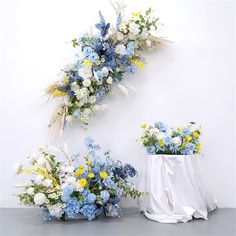 two white vases with blue and yellow flowers next to each other on a table