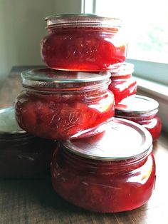 several jars filled with red liquid sitting on top of a wooden table next to a window