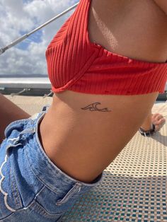 a woman with a small wave tattoo on her lower back ribcage, sitting on the beach