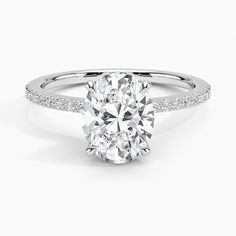 an oval cut diamond engagement ring with side stones on the band and shoulders, set in 18k white gold