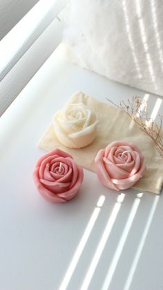 three small pink and white roses sitting on top of a piece of paper next to a window