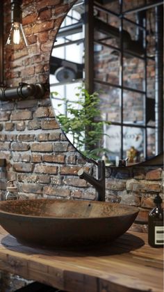 a bathroom sink sitting on top of a wooden counter next to a brick wall with a round mirror above it