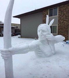 a snow sculpture of a person holding a pole in front of a house on a snowy day