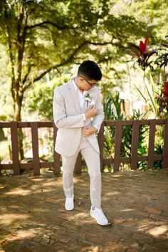 a man in a suit and white shoes standing on a brick walkway with trees in the background