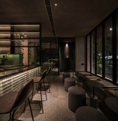 a dimly lit bar with stools and tables in front of large windows at night