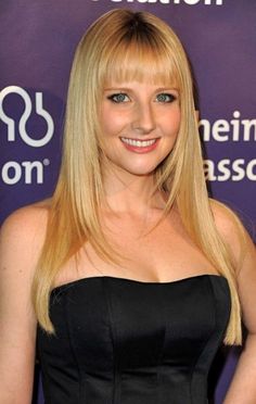 a woman with long blonde hair wearing a black dress and smiling at the camera while standing in front of a purple backdrop