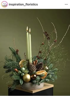 a christmas arrangement with pine cones, evergreens, candles and other holiday decorations on a table