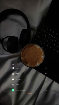 a laptop computer sitting on top of a bed next to headphones and a cup of coffee