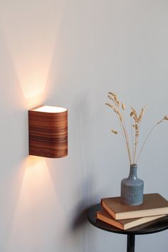 a wall light that is on the side of a wall next to a vase with flowers