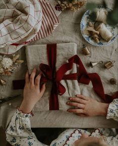 a person wrapping a gift on top of a table next to other christmas decorations and gifts