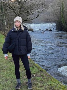 a woman standing next to a river with a waterfall in the background