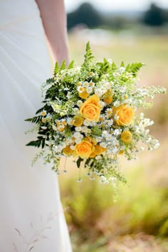 a bridal holding a bouquet of yellow roses and white daisies in the grass