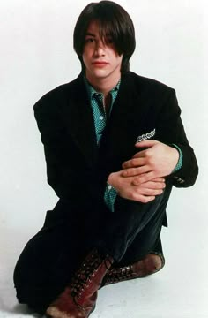 a man in a suit and tie sitting on the ground with his hands folded up