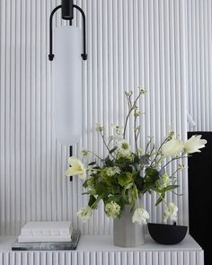 a vase filled with flowers sitting on top of a white shelf next to a lamp