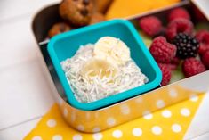 a lunch box with fruit, muffins and other foods in it on a yellow and white tablecloth