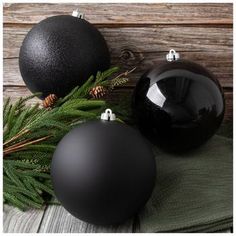 two black christmas ornaments sitting on top of a wooden table next to pine cones and evergreen needles