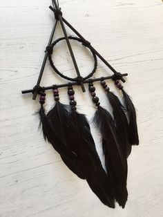 a black dream catcher with feathers hanging from it's side on a white table