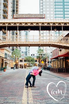 a man holding a woman in his arms on the street with an arch above him