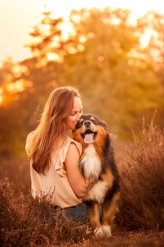 a woman holding a dog in her arms while sitting on top of a grass covered field