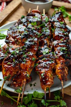 chicken skewers with sauce and parsley on a white plate next to a bowl of dipping sauce