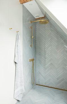 a bathroom with white walls and gold fixtures on the shower head, along with herringbone tile flooring