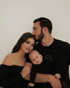 a man and woman holding a baby while posing for a photo with their arms around each other