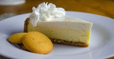 a piece of cheesecake on a white plate next to two cookies and whipped cream