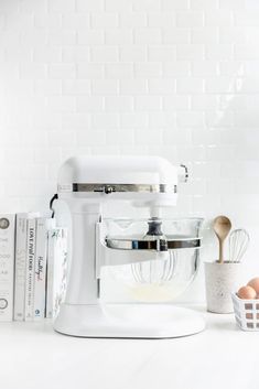 a white mixer sitting on top of a counter next to some books and an egg