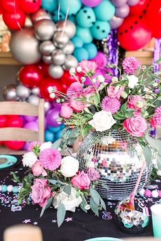 a disco ball centerpiece with pink and white flowers on a table surrounded by balloons