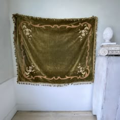 an old blanket hanging on the wall next to a white cabinet and marble busturine