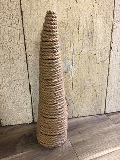 a rope wrapped vase sitting on top of a wooden floor next to a white wall